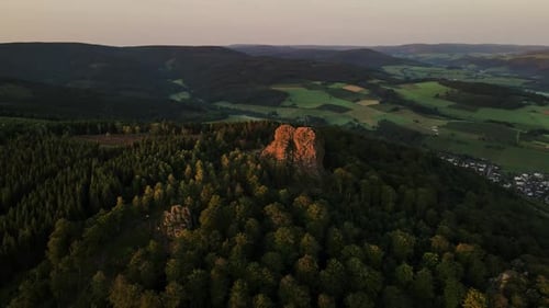 Drone shot wooded mountain and rocky mountains in a pine forest on a sunny evening