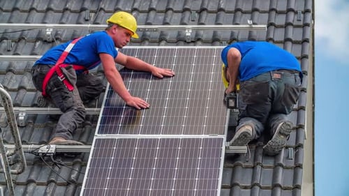 Two workers installing PV (Photovoltaic) solar panels on house roof for producing solar power. Slow