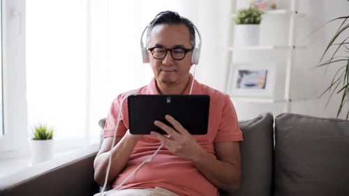 Happy Man with Tablet Pc Computer and Headphones Listening to Music At