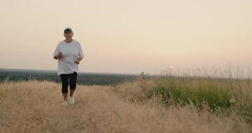 An Elderly Woman Runs Along a Country Road Goes in for Sports Rear View Active Seniors