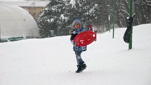 A happy child runs through the snow, sleds in hand, eager to reach the top of the hill