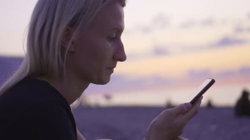 Woman Using Mobile Phone on the Beach at Sunset