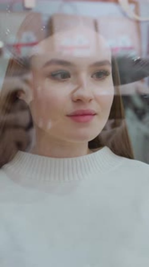 Woman Observing Display Through Glass in Mall with Reflections and Shoppers Passing