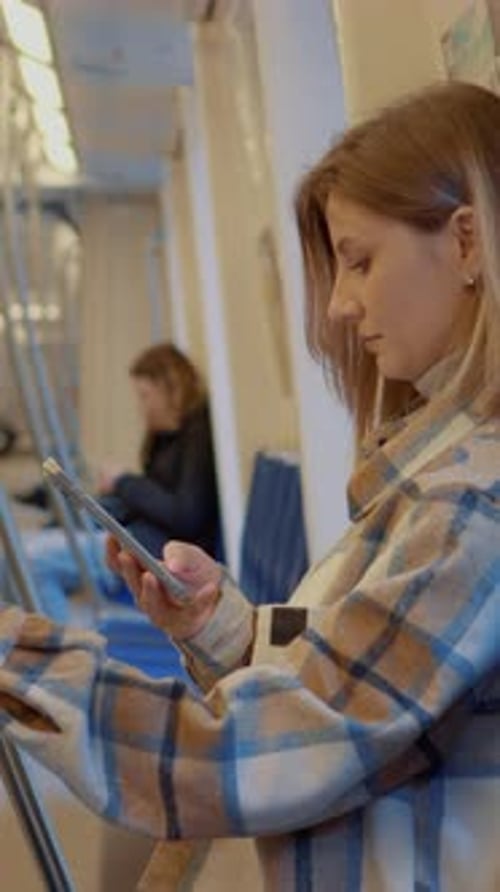 Vertical Screen Young mother using smartphone while traveling on subway with baby stroller