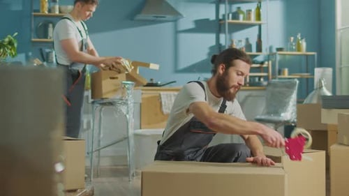 Worker of Moving Company Using Duct Tape Machine for Packing a Cardboard Box