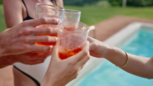 Group of friends cheer and cling glasses of refreshing drink or cocktail by pool in summer vacation