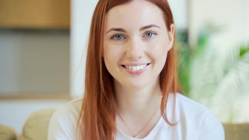 Close-up portrait of a redhaired young happy girl or woman happily smiling in living room at home.
