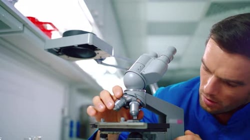 Man Examining Sample with Microscope in Bright Lab