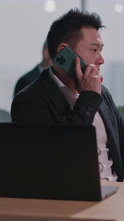 A Man in a Suit Talks on His Cell Phone at a Modern Office Desk