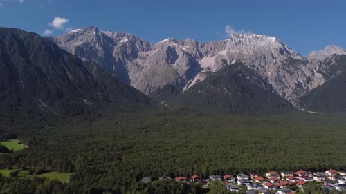 Drone flying sideways to the right along a massive Alp mountain side view with woods and houses in E