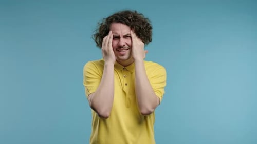 Young Curly Haired Man Having Headache Blood Pressure Studio Portrait Guy Putting Hands on Head