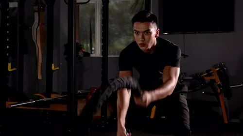 Leistungsstarker, muskulöser Sportler, Bodybuilder, macht Übungen mit Battle Ropes, intensives Fitnesstraining (z.