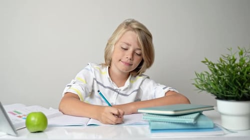 Middle School Smiling Student Boy Sitting at Desk Studying Writing Book Homework and Tablet at Class
