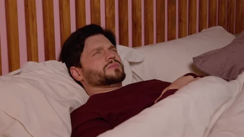 Un homme d'âge moyen endormi perturbé par le bruit se couvre la tête avec un oreiller dans son lit