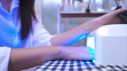 A customer is using a nail dryer after the manicurist coats the customer's finger nails.