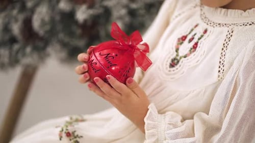 Slow-motion shot of Young girl in a Christmas ornamented white dress holding a red bauble - close up