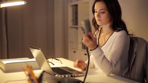 Woman working at night using laptop and phone