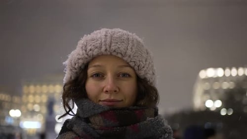 Woman in Hat Smiles as Snow Falls in City