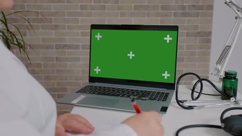 Healthcare worker hands writing treatment with a chroma key green screen laptop.