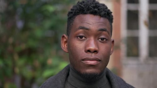 Confident young black man standing outside staring camera portrait face close-up