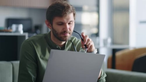 Young Man Using Laptop Indoors, Looking Concerned