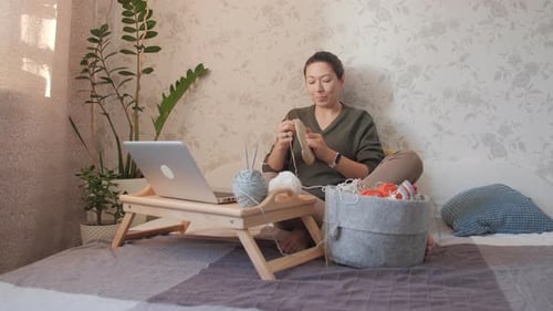 Woman Crafts with Yarn While Using Laptop