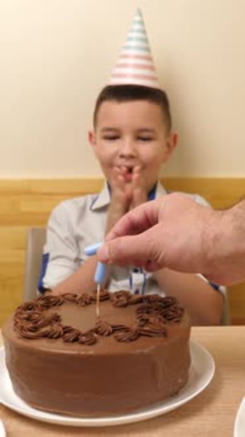 02. A boy is sitting in front of a table with a birthday cake, into which a candle in the form of th