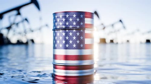 The camera zooms in on black barrels of oil or fuel and the US flag. A barrel of oil depicting the U