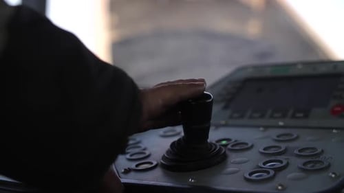 Hand of heavy equipment operator using joystick inside cabin of road paving machine