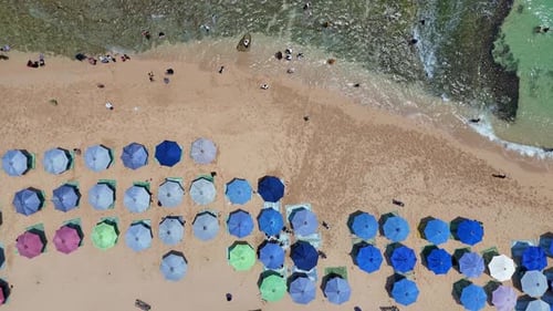 Aerial top-down view of colorful beach umbrellas arranged neatly on a sandy shore
