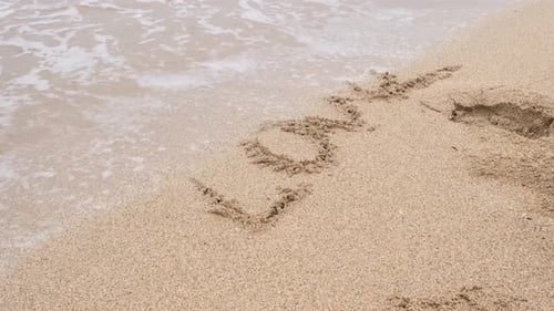 Geschriebenes Wort LIEBE auf Sand, der von Wellen weggespült wird
