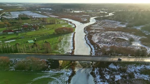 Aerial view of traffic driving over a bridge over a frozen river during sunrise.