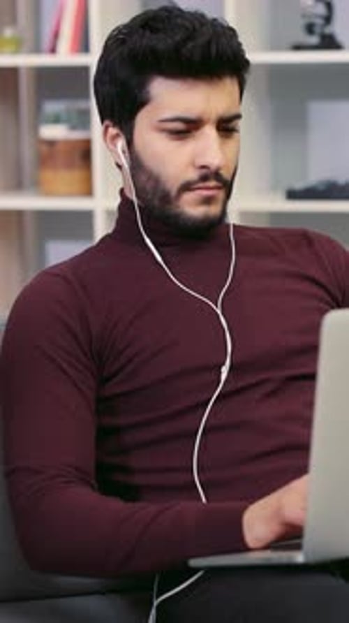 A Man with Headphones Works on a Laptop Showcasing Remote Productivity