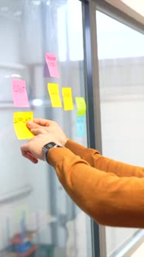 Hand Organizes Sticky Notes on Glass Wall