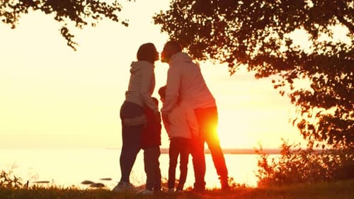 Affectionate Family Silhouetted at Sunset on Ocean Shore