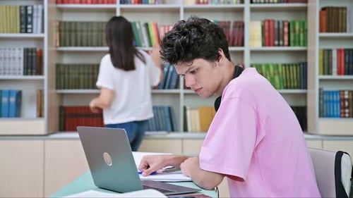 Young Male Student Sitting with Laptop with Books in College Library
