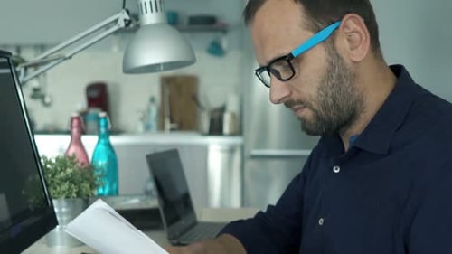 Man Reviews Business Documents at Home Office Desk