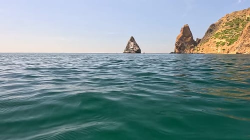 Sea Water Surface Camera Flies Over the Calm Azure Sea with Volcanic Rocky Shores on Background