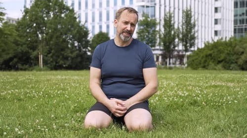 A Handsome Middleaged Caucasian Man Talks to the Camera As He Kneels on Grass in a Park