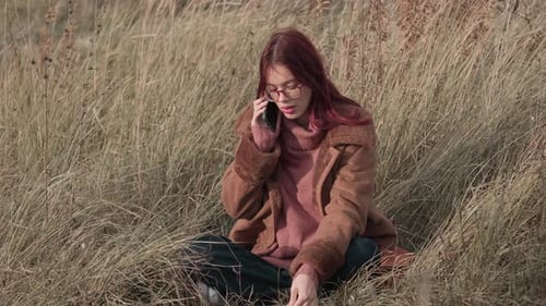 Teen Girl with a Serious Expression Talking on Her Phone Sitting in Tall Grass