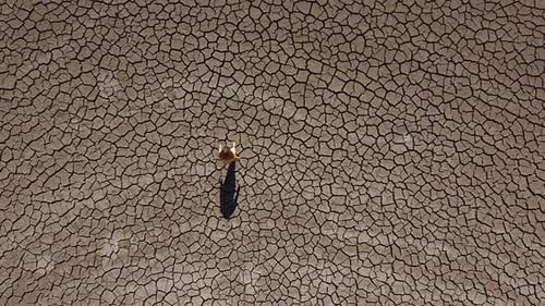 Weitwinkelaufnahme eines Mädchens, das während einer Dürre auf Zypern alleine durch eine trockene, karge Landschaft geht,
