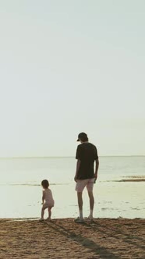 Vertical Video A Father and His Child Joyfully Walking Along the Beach During a Beautiful Sunset