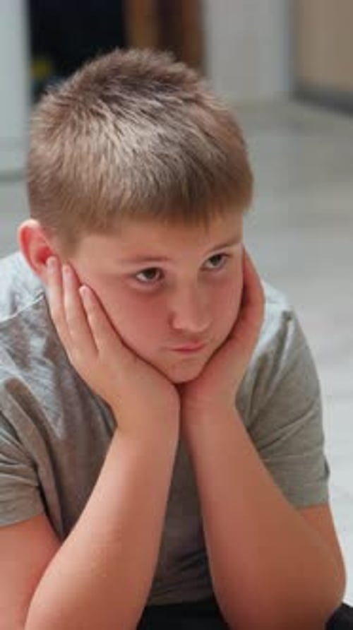 Young Male with Gray Clothing Shows Calm Introspective Mood Male Child Seated Indoors Displays