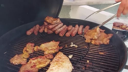 Taking off minced meat fingers called cevapcici from charcoal grill with steel clamps.