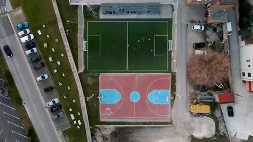 Drone flight from bird's eye view over a small soccer field next to an basketball field where a game
