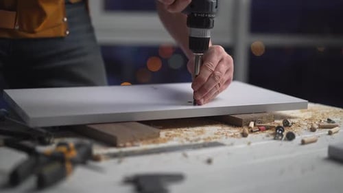 Tradesman Drilling Wood at Workbench at Night