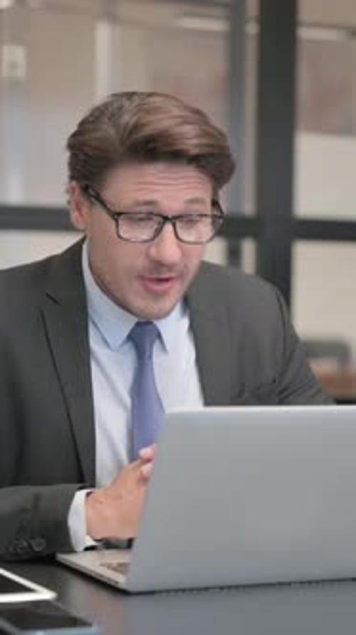 Businessman Chatting Online on Laptop while Sitting in Office, vertical