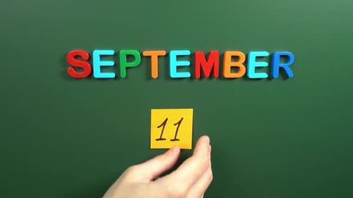 Hand sticking a sticker 11 september calendar day on school board. 11 date of september. Eleventh