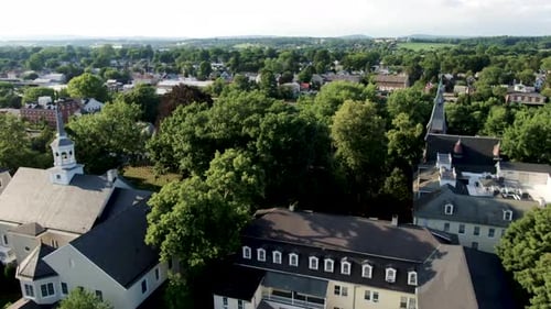 Aerial above church steeple, revealing small town with parade and people lining street in Lititz Pen