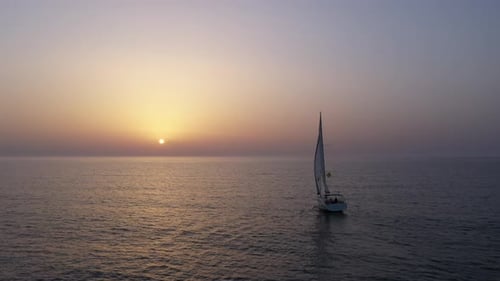 Sail boat sailing slowly towards a setting Sun in the Mediterranean Sea.